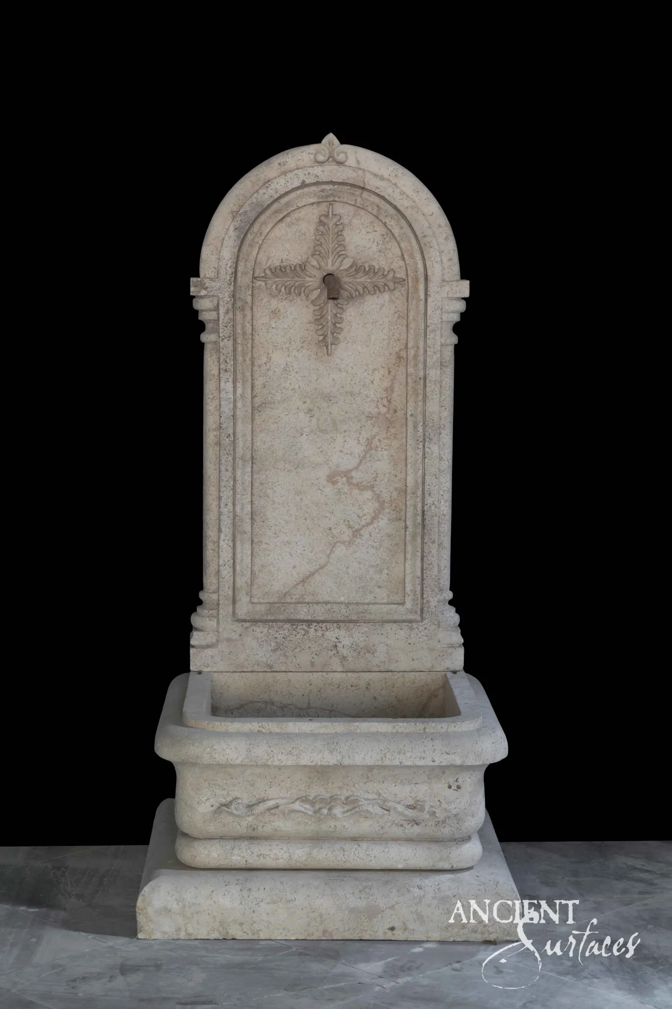 Tall arched cream limestone wall fountain with a carved finial and rectangular basin